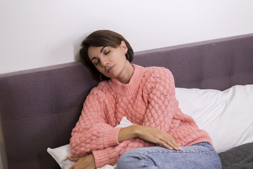 Règles abondantes et douloureuses : une femme épuisée au lit serrant un oreiller, en illustration des solutions pour soulager la douleur et la fatigue menstruelle.